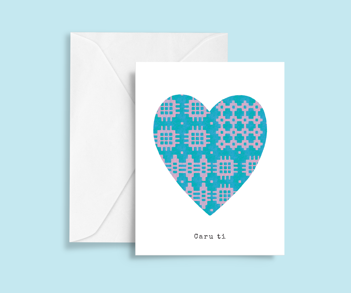 A minimalist romantic card featuring a blue and lilac Welsh blanket patterned heart in the centre with typewriter-style 'Caru ti' text below. Meaning Love you.
