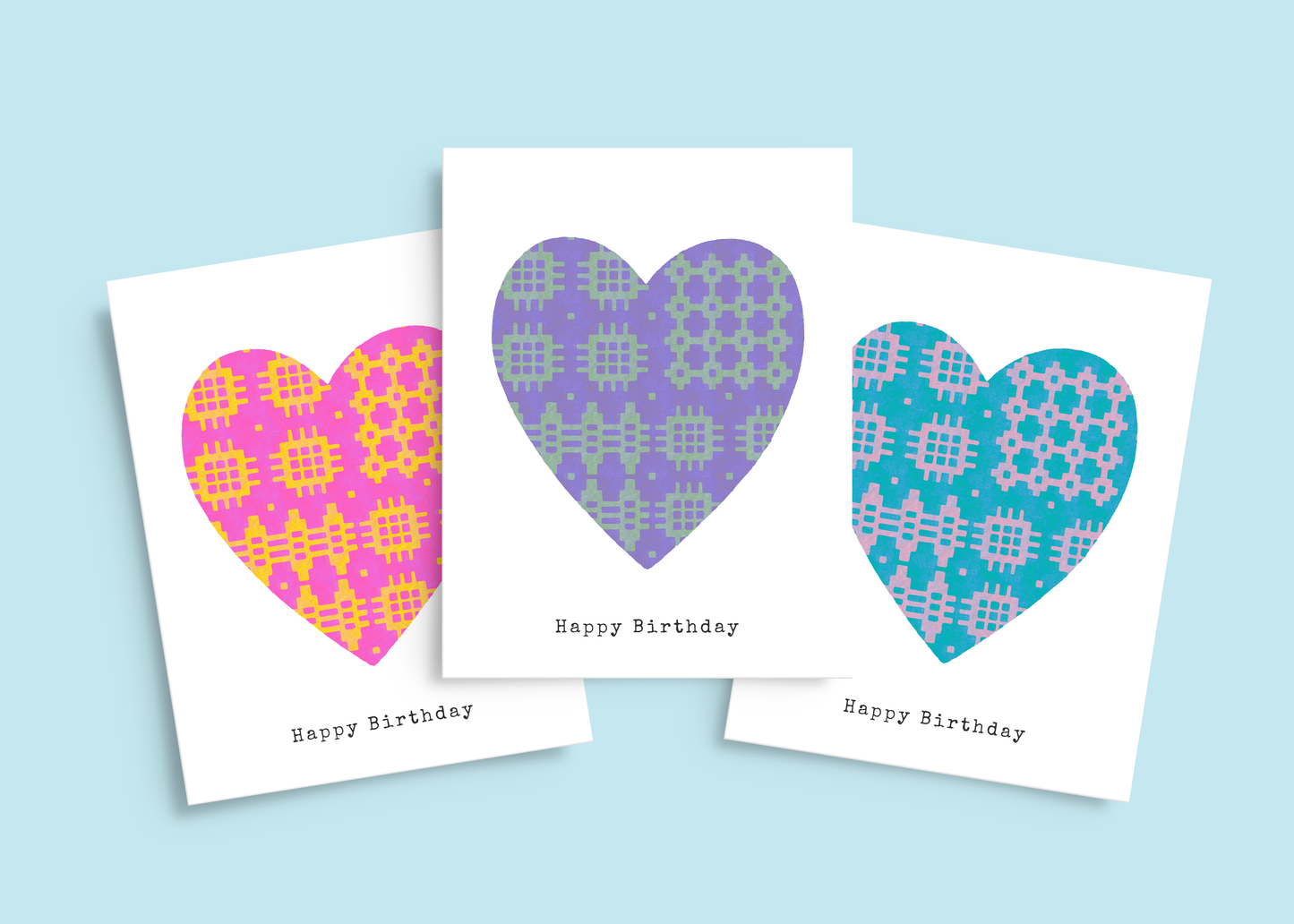 Set of three Welsh birthday cards in pink & yellow, purple & green, and blue & lilac, all featuring traditional blanket pattern hearts