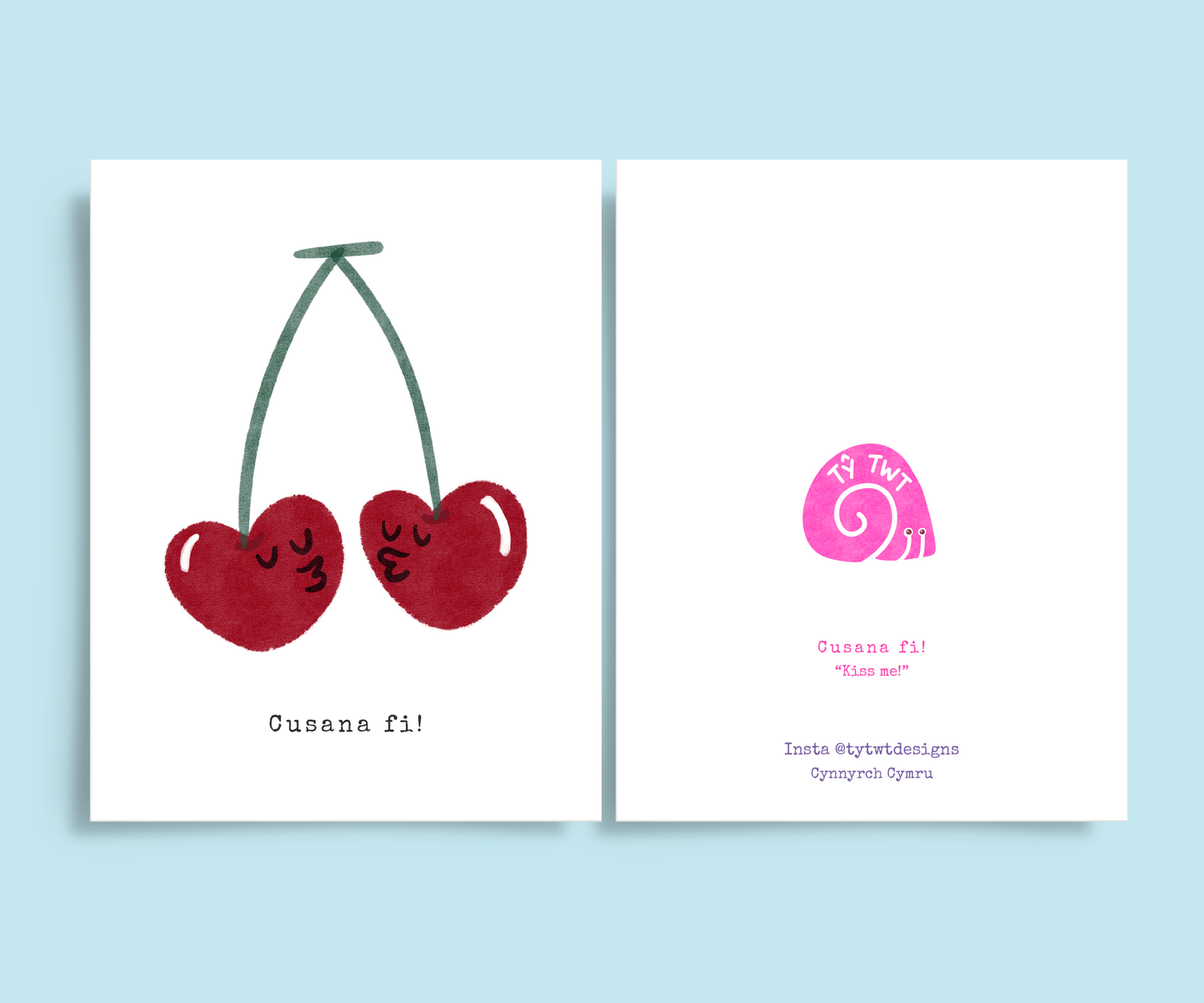 Both sides of romantic greeting card. Right is front of card with hand drawn print two cherries with faces kissing. Typewriter text below reads Cusana fi, Welsh for Kiss me. Left is back of card with translation and @tytwtdesigns