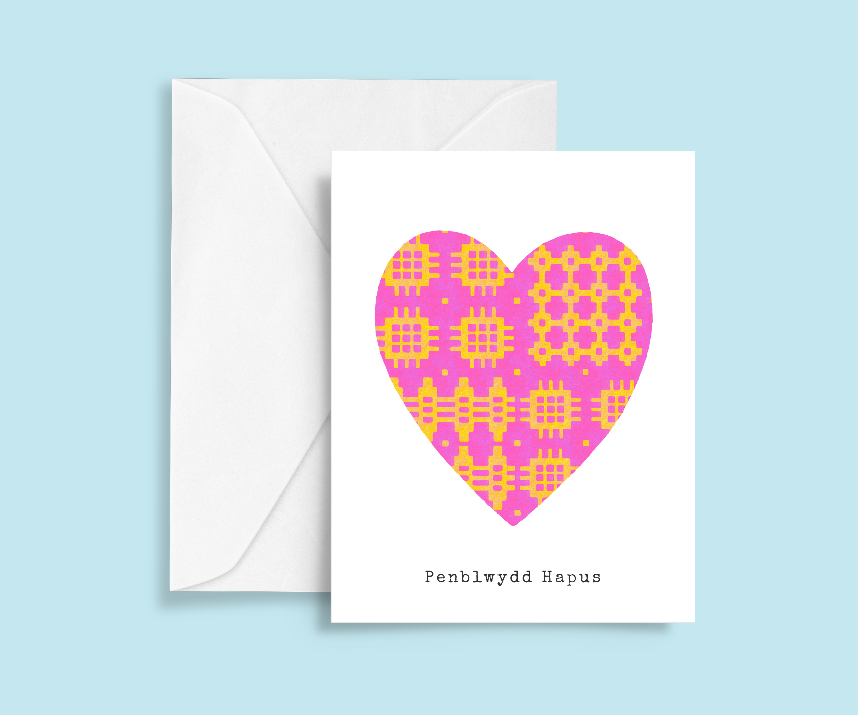 A minimalist Welsh birthday card featuring a pink and yellow Welsh blanket patterned heart in the center, with typewriter-style 'Penblwydd Hapus' text below. 