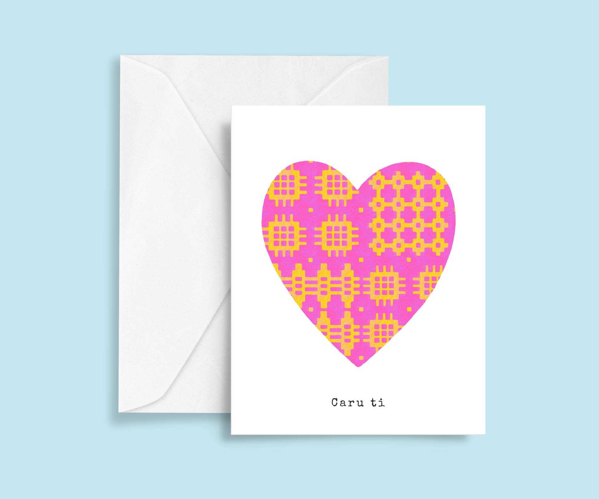A minimalist romantic card featuring a pink and yellow Welsh blanket patterned heart in the centre with typewriter-style 'Caru ti' text below.  Meaning Love you.